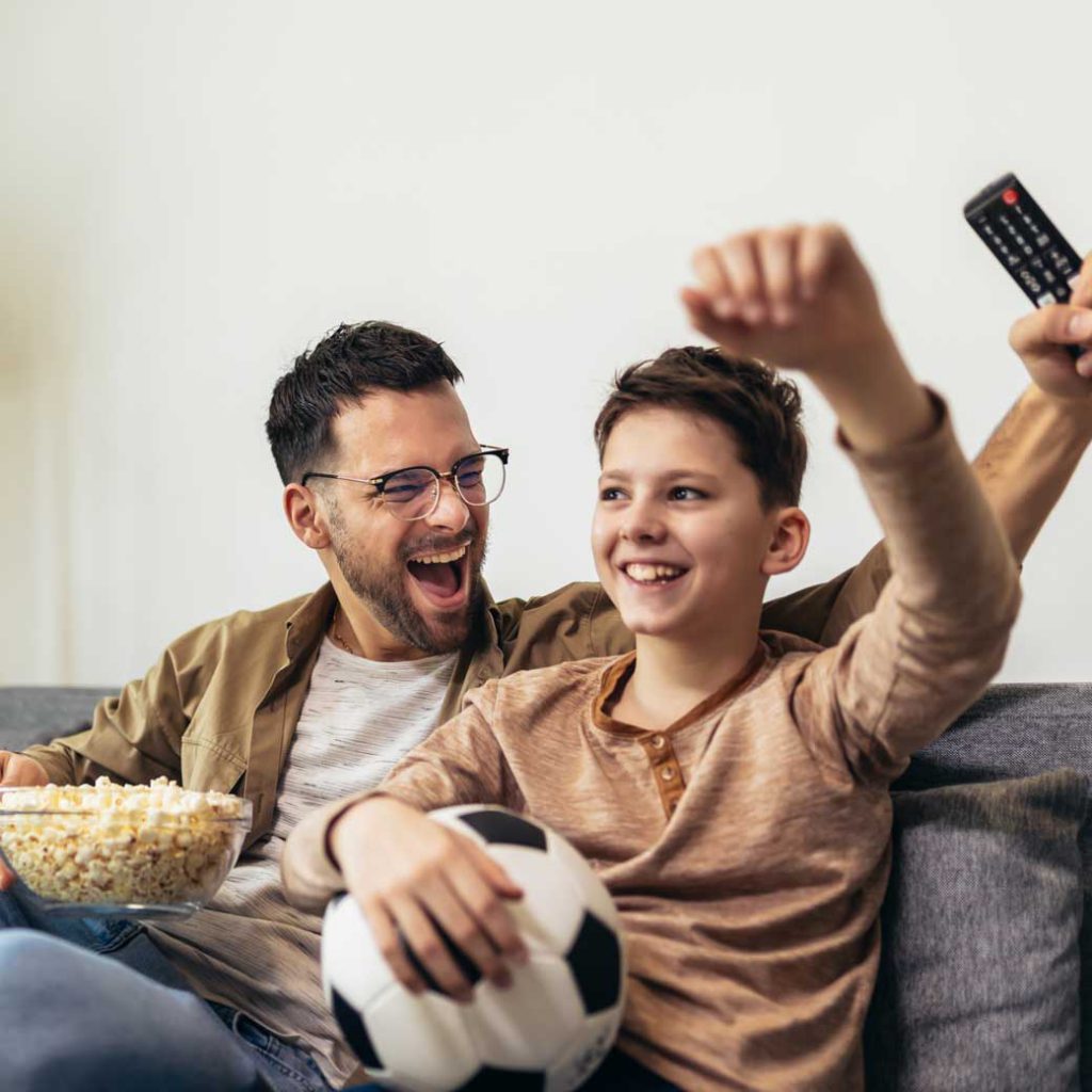 Padre e hijo en casa viendo partido futbol en TV.