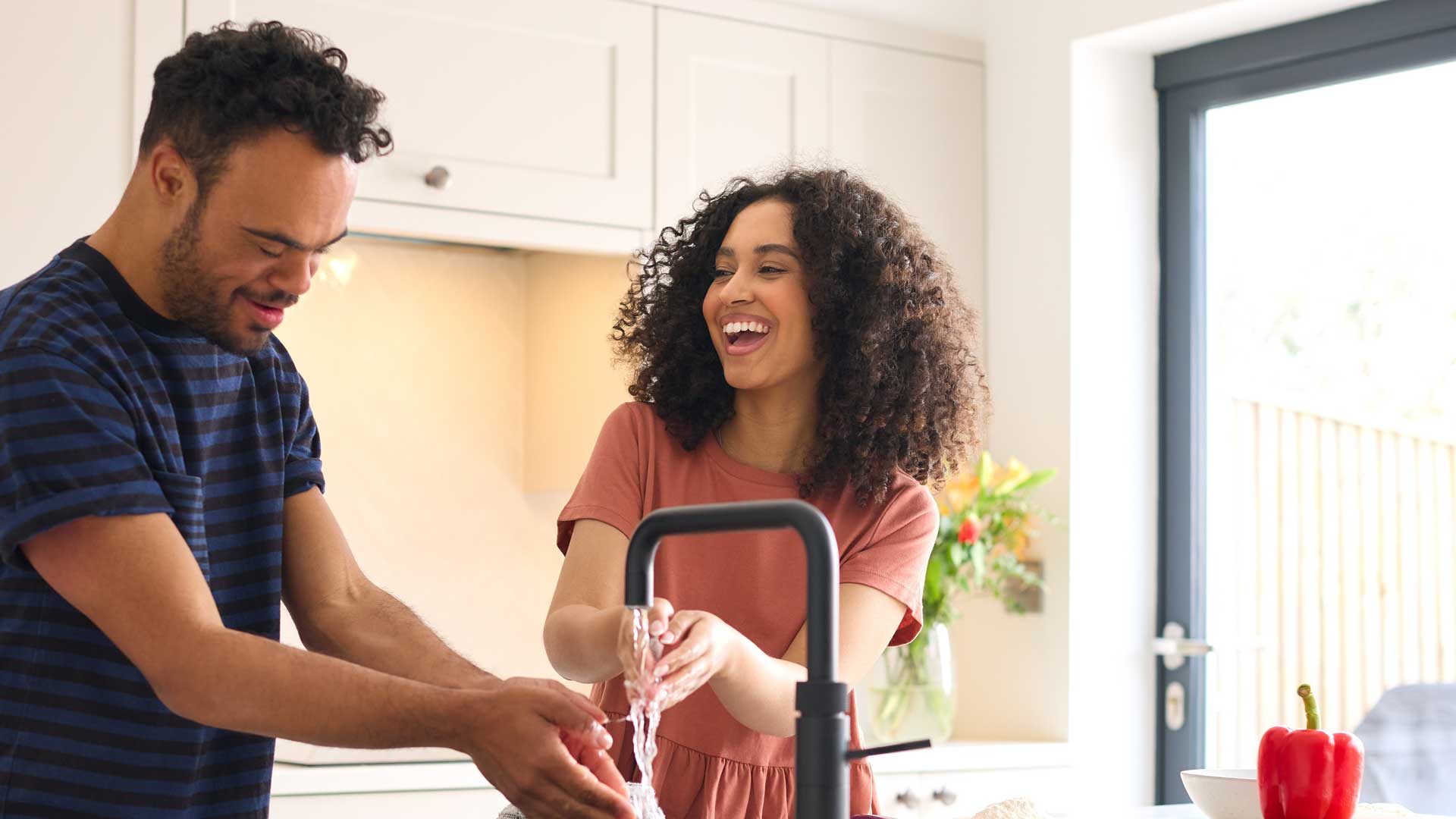 Pareja en casa con hombre con síndrome de down y mujer lavándose las manos antes de preparar la comida en cocina